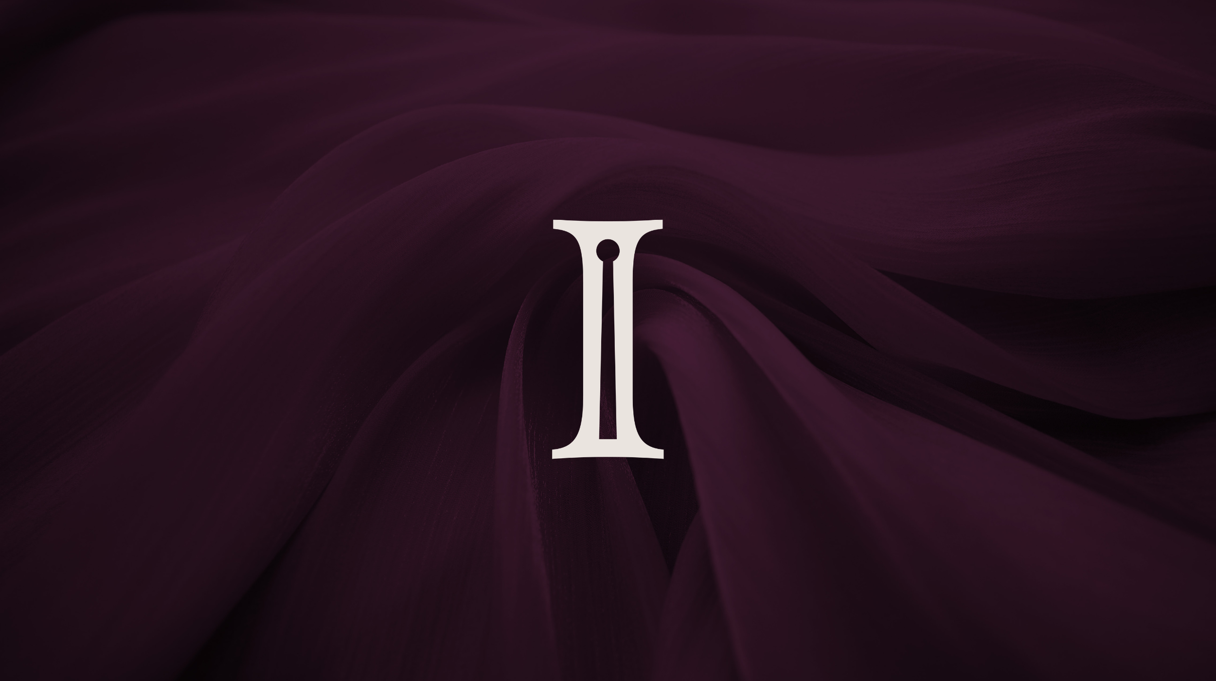 White Indulgent Interiors logo on a dark purple fabric background